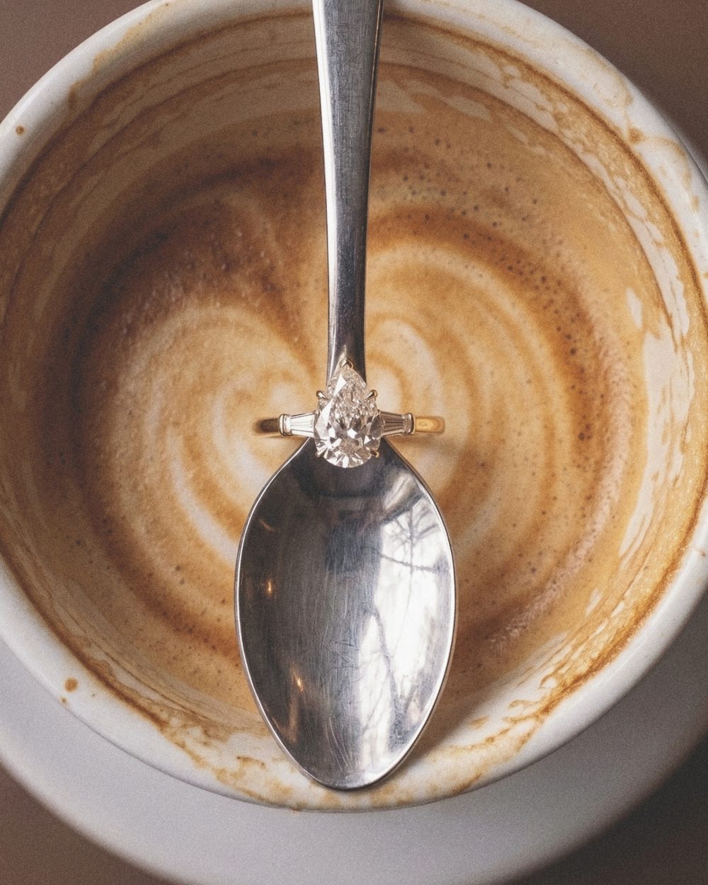 A diamond ring resting on a spoon in a coffee cup