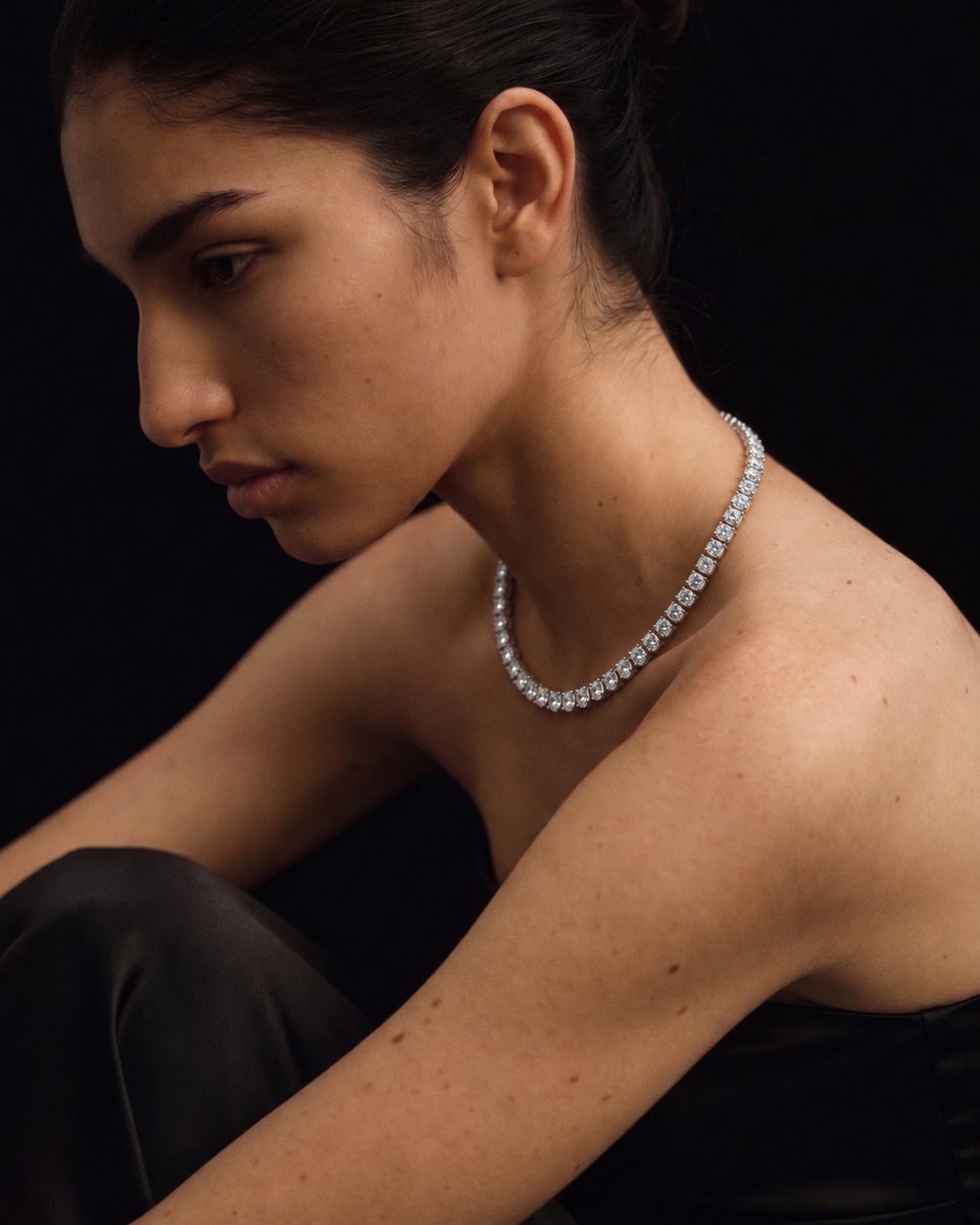 A model wearing a diamond necklace against a dark background